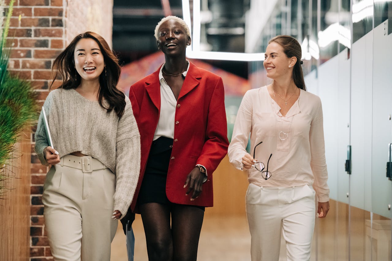 Home Three diverse and confident businesswomen walking together in a modern office hallway, exuding professionalism and joy.