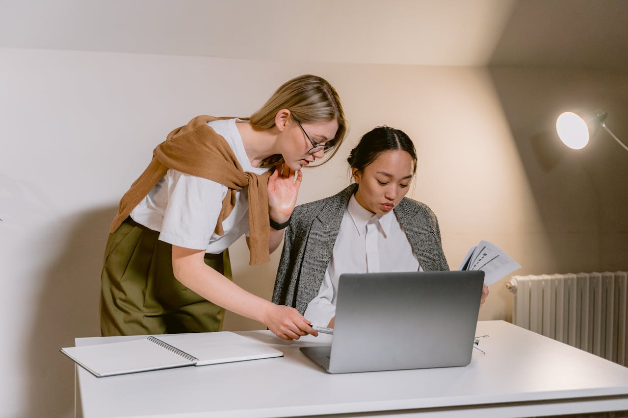Two women collaborating at a desk with a laptop and documents in a modern office.